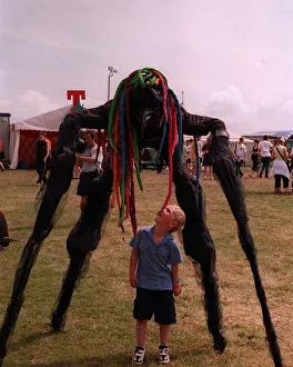 Stilted figure towering over a small boy at T in the Park wearing a bright coloured wig Stilted figure towering over a small boy at T in the Park wearing a bright coloured wig
