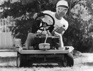 Stirling Moss sitting on lawn mower wearing crash helmet Stirling Moss sitting on lawn mower wearing crash helmet