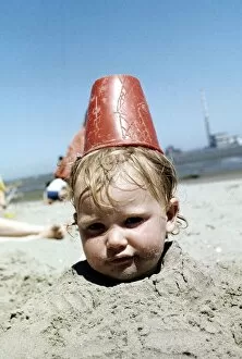 Summer holidays July 1976 - Boy buried in sand with red plastic Bucket on his head