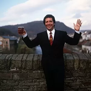 Tom Jones Singer in his home town in Wales standing by brick wall holding pint glass of