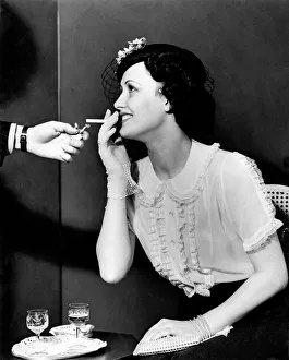 A woman about to smoke a cigarette, receives a light from a man A woman about to smoke a cigarette, receives a light from a man