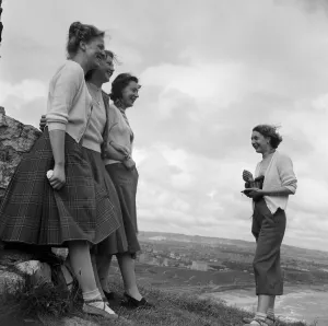 A woman taking a photograph of three women, in a coastal area, North Yorkshire A woman taking a photograph of three women, in a coastal area, North Yorkshire