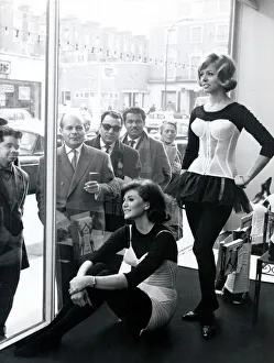Two women modelling corsets in shop window while people on the street look in - March Two women modelling corsets in shop window while people on the street look in - March