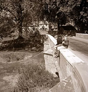 Two young boys sitting on the side of a bridge as they try fishing in their local river Two young boys sitting on the side of a bridge as they try fishing in their local river