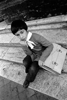 Young child sitting on the steps of his school in a poor suburb on the outskirts of Rome