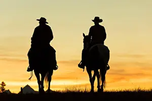 Two cowboys riding on horseback in a Prairie landscape at sunset