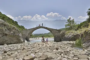 Prints of Two young woman walking barefoot in the riverbed over large stones, Ottoman stone bridge, Kadiut Bridge, Lengarica Canyon, Benje, Albania Albania Prints: Albanian Landscape Print: Kadiut Bridge and Lengarica Canyon